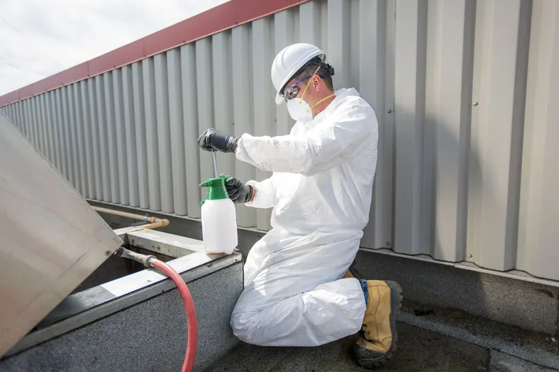 Technician in a hard hat kneeling on a commercial roof beside an opened exhaust fan housing