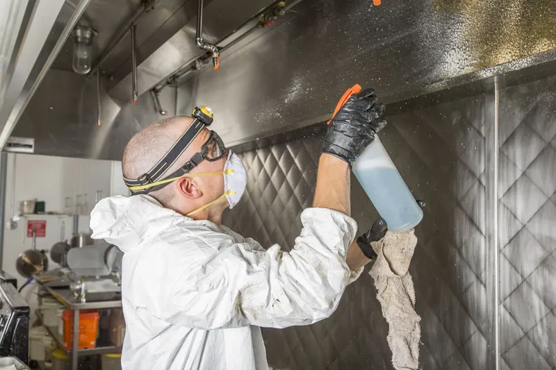 Technician spraying degreaser on the quilted stainless wall under a kitchen exhaust hood