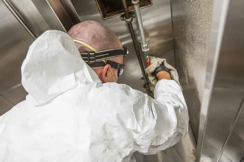 Technician wiping grease from a pipe and wall behind a commercial kitchen hood