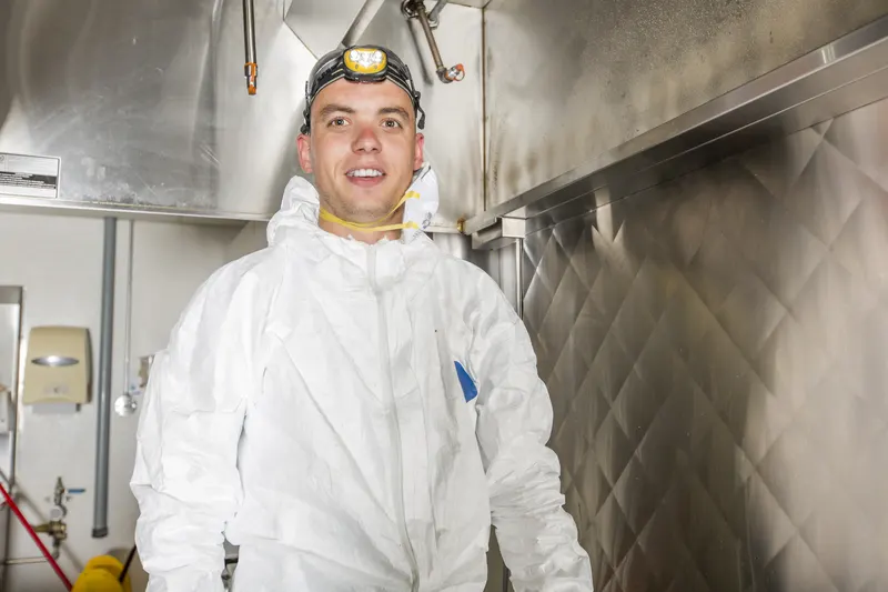 Hood cleaning technician in protective coveralls and respirator standing in a commercial kitchen
