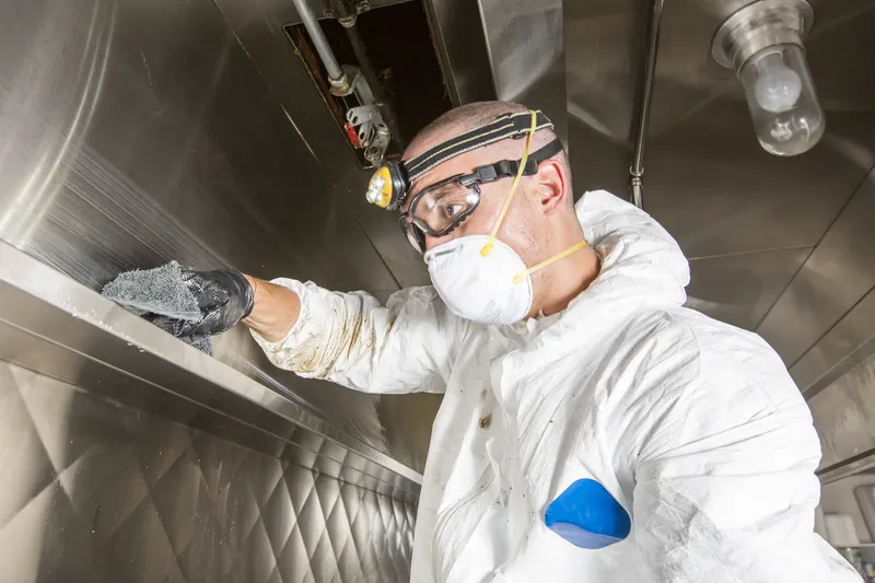 Technician wiping the inside ledge of a commercial kitchen hood beside the hood light